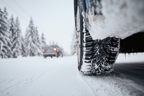 Winter Tires vs. All-Season: Why Should I Get Winter Tires? with Bock Auto in Amagansett NY; image of snow covered roads and evergreen trees with cars driving and closeup of snow tires on car