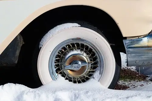 8 Best Winter Storage Practices for Classic Cars | Bock Auto in Amagansett, NY. Closeup image of a classic white car with a wheel covered by snow cover in winter.