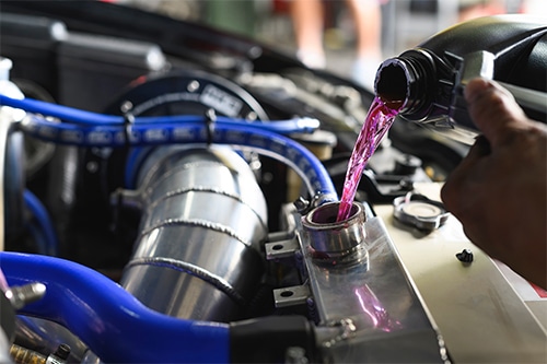 Auto mechanic pouring coolant fluid into a radiator fill hole. Concept image of fluid services a Bock Auto in Amagansett, NY.