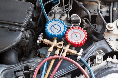AC repair and maintenance in Amagansett, NY at Bock Auto. Image of a mechanic using a measuring manifold gauge to check for leaks, detect issues, and fill a car's air conditioner to repair the heating and cooling system.