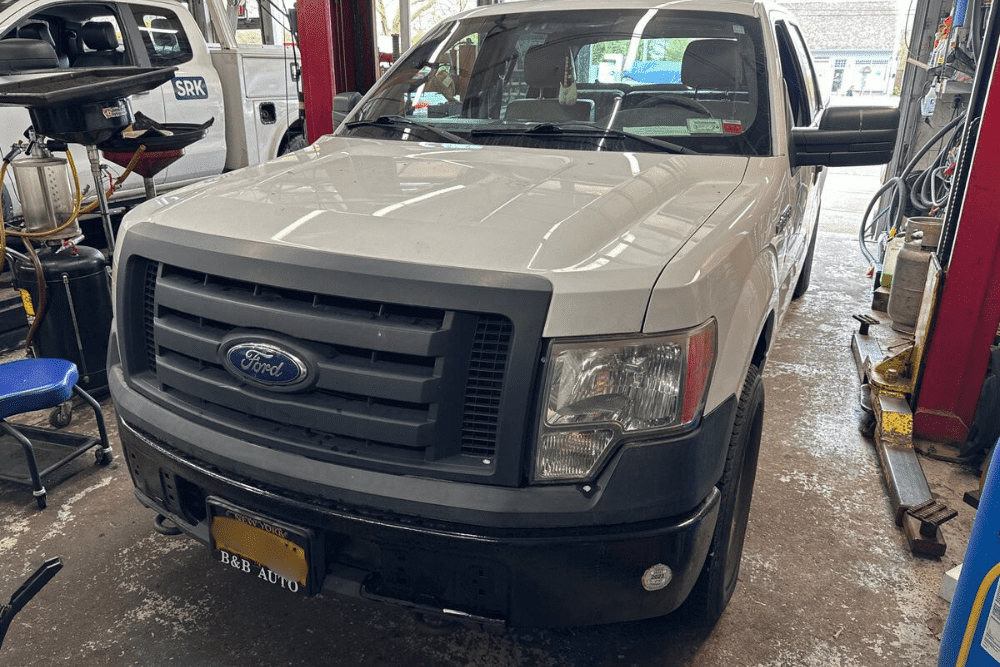 Ford pickup truck inside Bock Auto’s repair shop in Amagansett, NY, undergoing factory scheduled maintenance with nearby tools and equipment visible in the background.